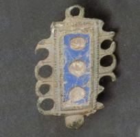 FIB-4697 - Fibule émailléebronzeFibule rectangulaire comportant une loge centrale d'émaux avec pastilles de verre incrustées, et de part et d'autre une bordure ajourée de cercles; bouton au pied et anneau percé au sommet; charnière à deux plaquettes.