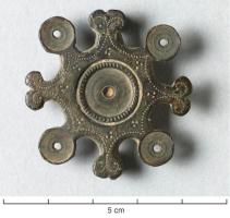 FIB-4746 - Fibule géométrique platebronzeFibule plate, dont la charnière disposée au revers comporte deux plaquettes coulées reliées par un axe en fer. Variante radiée avec alternativement des fleurons bifides et des cercles ornés de rondelles d'os tourné; même décor au centre, avec en entourage le classique cercle concentrique avec un motif perlé; dans la zone intermédiaire, décor poinçonné d'inspiration végétale.