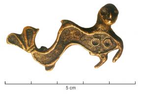 FIB-4936 - Fibule zoomorphe : sirènebronzeFibule zoomorphe associant un corps de poisson, ondulant, équipé de nageoires et terminé par une queue bifide également émaillée, à une tête humaine en ronde-bosse et deux seins figurés par des pastilles émaillées en champlevé. Les deux pattes ou bras antérieurs sont figurés.