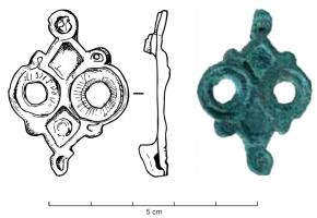 FIB-4984 - Fibule symétrique émailléebronzeFibule plate, à corps de forme générale losangique entièrement émaillé; les angles latéraux sont remplacés par des anneaux dentelés; les deux pointes restantes sont prolongées par des disques émaillés
