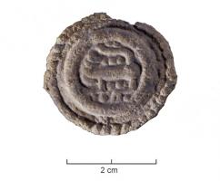 FIB-6055 - Fibule discoïde : monstre à tête retournéeplombMédaillon plat, coulé d'un seul tenant, portant un motif animalier en relief dans un cercle de filets guillochés ; au revers, bélière percée pour maintenir le système d'ariculation, et porte-ardillon en crochet.