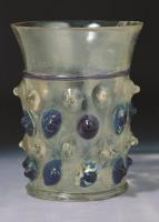 GOB-7005 - Nuppenbecher à gouttes bleuesverreGobelet en verre incolore et gouttes rapportées, alternant des gouttes en verre incolore et en verre bleu. La base est généralement soulignée par un élargissement, soit sous la forme d'une couronne rapportée, soit par écrasement de la base repoussée. La lèvre est évasée et soulignée d'un filet bleu.