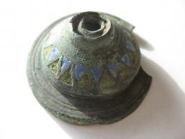 IND-4157 - Pied émaillébronzePied associant un piètement circulaire et une sorte de coque creuse, ornée sur les flancs extérieurs d'une alternance de triangles émaillés. Le sommet perforé comporte un arrachement  indiquant un prolongement tubulaire.