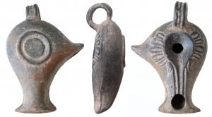 LMP-3017 - Lampe delphiniforme à cols de cygneterre cuiteLampe moulée, anse verticale en ruban à deux cannelures, rapportée. Réservoir de profil biconique, poucier en forme de corne saillante à gauche. Couronne d'oves allongés sur le bandeau. Disque en simple cuvette ouverte sur un étroit canal bordé de deux cols et têtes de cygne stylisés. Bec en enclume.  Base circulaire plate, limitée par un bourrelet entourant un rond en relief.  Vernis noir brillant.