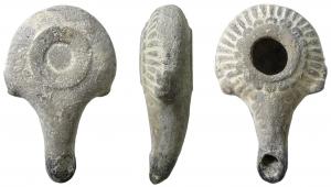 LMP-3075 - Lampe hellénistique moulée à deux pouciers en Sterre cuiteRéservoir circulaire de profil biconvexe porte un poucier en S des deux côtés.  Grand trou d'alimentation entouré d'un anneau plat en relief. Bandeau décoré des stries rayonnantes et d'une couronne d'oves simples autour du trou d'alimentation. Bec long, tubulaire, étroit, au bout arrondi. restes d'une palmette sur le dessus. Base circulaire en anneau en léger relief. 