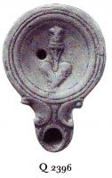 LMP-41065 - Lampe à bec en ogive à volutes doubles : Tropaionterre cuiteLampe moulée à bec en ogive à deux volutes doubles se poursuivant sous le bec. Sans anse. Disque en cuvette limitée par trois sillons concentriques. Bandeau plat. Réservoir circulaire à profil biconvexe. Base circulaire plate en léger relief limitée par un sillon. Décor : Tropaion, trophée destiné à commémorer une victoire militaire.