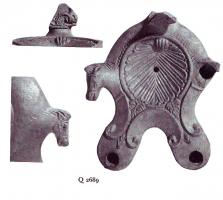 LMP-41187 - Lampe Loeschcke III à deux becs : feuilleterre cuiteLampe ronde à double bec à volutes avec terminaison en ogive et tête de cheval à la fin de chaque volute, sur le côté. Feuille en relief au début de chaque bec, et décoration entre les volutes vers le trou de mèche. Médaillon décoré d'une valve de coquillage. Anse plastique perdue.