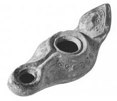 LMP-41486 - Lampe syrienne tardive terre cuiteLampe allongée à long bec avec canal, épaule décorée de motifs géométriques et anse plastique triangulaire décorée d'une tête barbue.