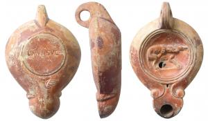 LMP-41544 - Lampe Loeschcke V : chiens, L MVN SVCterre cuiteAnse percée à deux sillons, moulée avec la lampe. Réservoir piriforme de profil biconvexe asymétrique. Bandeau penché vers l'extérieur. Disque circulaire limité par deux sillons. Décor : accouplement canin, à droite. Bec long en ogive, à volutes simples se poursuivant sous le bec.Trou d'évent. Base circulaire plate limitée par un sillon, estampillée L'MVN SVC, feuille triangulaire en creux sous le bec. Engobe rouge brique sur toute la lampe.  