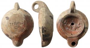 LMP-41578 - Lampe à bec rond limité par un trait : Dauphins, TARI FLOterre cuiteLampe moulée, anse verticale percée à deux sillons sur la tranche. Réservoir circulaire à profil biconvexe. Bandeau penché vers l'extérieur, disque en cuvette limitée par deux sillons concentriques. Décor : deux dauphins affrontés. Bec arrondi limité par un trait droit. Base circulaire plate en léger relief limitée par un sillon, estampillée TARI.FLO. cercle en relief en dessous. Restes d'engobe rouge marron  sur toute la lampe.