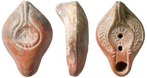 LMP-41658 - Lampe Hayes I : Rosaceterre cuiteLampe moulée, anse verticale pleine à un sillon, deux points au départ. Réservoir piriforme de profil biconvexe. Palme descendante sur le bandeau. Disque et  bec entourés par un bourrelet. Fleur stylisée sur le disque. Base concave limitée par un bourrelet souligné par une gouttière. Forme patère avec l'anse. porte un élément en forme de flèche. Engobe rouge orangé.