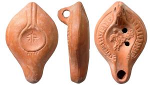 LMP-41663 - Lampe Hayes I : Cavalierterre cuiteLampe moulée, anse verticale percée à un sillon, faisant avec la patère une excroissance caractéristique du type. Réservoir piriforme de profil biconvexe. Alternance de rayons creux et de rectangles striés sur le bandeau entourés par un sillon. Bec moyen et  disque entourés par un bourrelet.: cavalier sur sa monture à gauche. Base plate limitée par un bourrelet. double bourrelet rejoignant l'anse, l'ensemble formant une patère. Porte un arc et sa flèche gravés. Engobe rouge orangé brillant.