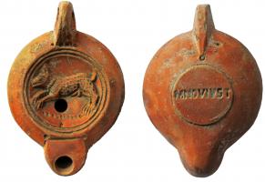LMP-41999 - Lampe à bec rond limité par un trait : Chien, M NOV IVSTterre cuiteLampe moulée, anse verticale percée à deux sillons sur la tranche, 4 points au contact du réservoir, circulaire à profil biconvexe. Bandeau lisse penché vers l'extérieur, disque en cuvette limitée par deux sillons concentriques. Décor : Chien courant à gauche, avec collier. Bec arrondi limité par un trait droit ponctué aux extrémités. Base circulaire plate en léger relief limitée par un sillon, estampillée MNOVIVST. Engobe orangé rouge sur toute la lampe.