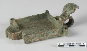 LMP-42253 - Lampe à suifbronzeLampe ouverte, à fond plat et bords droits, évoquant peut-être un plan basilical à abside : simple rectangle avec un bec en arc de cercle à l'opposé d'une anse à réflecteur en forme de feuille surmontant un anneau.