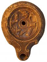 LMP-4303 - Lampe Loeschcke IV : Armes de gladiateursterre cuiteLampe à bec en ogive et volutes latérales; disque orné d'une frise d'armes de gladiateurs. Argile noisette, engobe orange foncé à marron foncé; base plate entourée d'un anneau en relief.