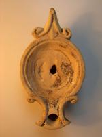 LMP-4308 - Lampe Loeschcke I terre cuiteLampe à bec à enclume et volutes latérales; disque vierge. Argile noisette, engobe orange foncé à marron foncé; base plate entourée d'un anneau en relief. Anse horizontale triangulaire à  volutes.