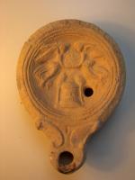 LMP-4317 - Lampe Loeschcke IV : Victoires autelterre cuiteLampe à bec à ogive et volutes latérales; disque orné de deux victoires survolant un autel. Les victoires tiennent un disque. Argile beige, engobe perdue; base plate définie par un cercle incisé; cassure au fond.