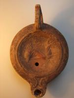 LMP-4319 - Lampe Loeschcke V : Poisson et trident, Hterre cuiteLampe à bec à ogive et volutes intégrées dans l'épaule; disque orné d'un poisson chevauchant un trident, vers la gauche. Argile beige, engobe marron foncé; base plate entourée d'un anneau en relief.