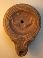 LMP-4320 - Lampe Loeschcke IV : Poissons Hterre cuiteLampe à bec à ogive et volutes intégrées dans l'épaule; disque orné de deux dauphins affrontés ; base plate entourée d'un anneau en relief; au centre marque H incisée.