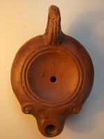 LMP-4321 - Lampe à bec rond orné de volutes: Iterre cuiteLampe à bec rond, variante égyptienne du type Loeschcke VIII à long bec surmonté d’un anneau en relief et demi volutes sur le côté. Médaillon légèrement concave, défini par deux anneaux en relief. Epaule convexe. Anse moulée, striée, percée, à l’arrière. Base plate entourée d’un anneau en relief ; au centre : lettre I incisée.