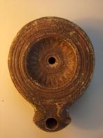 LMP-4358 - Lampe Loeschcke I, var. alexandrine : Rosette IVNEPI /S.terre cuiteLampe à bec à enclume (variante locale) surmonté de deux volutes en relief séparées par un canal. Médaillon concave, orné d’une rosette aux pétales jaillissant des deux cercles en fin relief entourant la zone du trou de remplissage. Epaule plate ornée de cercles concentriques incisés. Base plate définie par deux cercles incisés ; au centre, en lettres incisées et sur deux registres, on lit la marque IVNEPI /S.