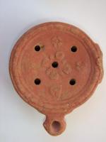 LMP-4408 - Lampe Mlynarczyk II.23 : Fleurs FILOIKOSterre cuiteLampe à bec en enclume; disque orné de 5 fleurs en relief. Argile orange clair, engobe perdue; base plate. Anse latérale (perdue). 5 trous de remplissage. Marque: FILOIKOS en lettres grecques incisées.