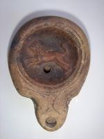 LMP-4444 - Lampe Loeschcke IV : Lionterre cuiteLampe à bec à ogive et volutes. Disque décoré d'un lion courant à gauche. Argile beige, engobe marron; base plate.