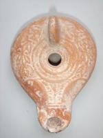 LMP-4700 - Lampe du Darom et de Gerasaterre cuiteLampe allongée, moulée, au réservoir aplati et à l’épaule bombée et au long bec en ogive. Un bourrelet circulaire en relief entoure un médaillon creux, vierge, percé en son centre par le petit trou de remplissage. Sur l’épaule, très convexe, on observe une couronne de myrte. A l’arrière, petite anse ronde, moulée mais non percée. Sur le début du bec, décor constitué d’une ligne verticale incisée se terminant en deux demi volutes joignant une ligne horizontale située au-dessus du trou de remplissage. Base plate entourée d’un anneau circulaire en faible relief et décorée en son centre d’un petit cercle en relief.