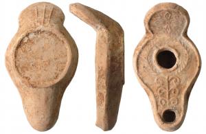 LMP-5024 - Lampe syro-palestinienneterre cuiteAnse ronde relevée portant  une alternance rayonnante de cercles pointés et de losanges formant une croix. Récipient piriforme plat de profil biconvexe asymétrique. Dessus plat sans bandeau. Un bourrelet entoure le tout ainsi que l'anse. Couronne de palme autour du grand trou d'alimentation entouré par un bourrelet. Bec long décoré de six volutes symétriques sur un axe vertical.  Grande base circulaire plate limitée par un bourrelet en relief.  Trois traits en relief sous l'anse. Restes d'un engobe rouge foncé sur toute la lampe.