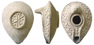 LMP-5036 - Lampe syro-palestinienne à canalterre cuiteAnse en tenon conique. Réservoir en amande de profil biconique. Altrenance  de cercles en relief et de globules sur le bandeau. Grand trou d'alimentation bordé par un bourrelet, entouré par une gouttière. Le bourrelet qui la limite se poursuit de long d'un canal sur le bec qui porte une palme stylisée. Base circulaire plate entourée par un bourrelet en relief contenant une croix aux branches en V ponctuées de globules.