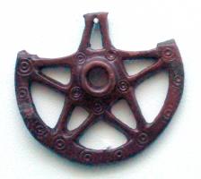 MRS-5002 - Aplique latérale de morsbronzeTPQ : 600 - TAQ : 712Applique latérale de mors évoquant la forme d'une roue avec son moyeu cylindrique; bélière trapézoïdale au sommet.