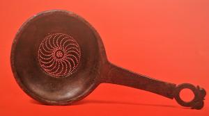 PAS-3003 - Passoire à manche coulébronzePassoire en bronze martelé, vasque hémisphérique avec au centre une cupule plus profonde qui est perforée pour filtrer le contenu; manche plat percé à son extrémité d'une ouverture ronde, deux ou trois ergots ergots autour de l'anneau.