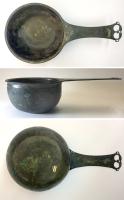 PAT-4090 - PatèrebronzePatère à panse renflée, lèvre moulurée, fond plat décoré de cercles concentriques; le manche plat est orné d'oves incisées près de la panse, et la terminaison percée de deux ajours en forme de pelte; parfois, décor figuré sur le manche, et / ou estampille rectiligne longitudinale.