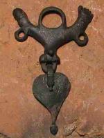 PDH-4073 - Pendant de harnais phalliquebronzePendant de harnais à anneau coulé, représentant des parties génitales masculines stylisées, au repos, encadrées par deux bras symétriques redressés vers le haut (un phallus dressé et une main faisant le geste de la figue) ; les trois éléments sont pourvus d'anneaux pour la suspension de pendants foliacés.