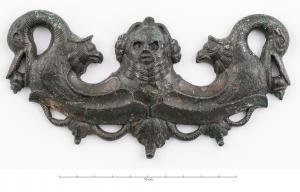 PGM-4020 - Poignée de meuble, buste de SilènebronzePoignée plate en forme d'oméga, jonc cannelé à revers creux, interrompu par un buste de Silène, placé entre deux têtes de griffons affrontées ; aux extrémités, têtes d'anatidés tenant dans leur bec une baie ou un gland.