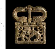 PLB-4009 - Plaque-boucle articulée à extrémités zoomorphesbronzePlaque boucle articulée, à boucle réniforme formée de deux têtes d'oiseaux aquatiques affrontées, et deux têtes de lion se faisant face de part et d'autre de la charnière; plaque ajourée avec une scène historiée : panthère attaquant un ours.