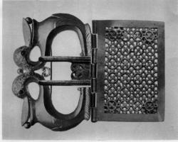 PLB-4075 - Plaque-boucle articuléeorBoucle de ceinture à deux ardillons, avec articulation à charnons multiples reliant la boucle avec une plaque rectangulaire entièrement ajourée en opus interrasile, dans un cadre lisse; 4 rivets de fixation au revers. La boucle se termine par deux têtes d'oiseaux aquatiques adossées, tenant une baie dans le bec, les yeux incrustés de grenats.