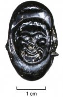 PRL-4008 - Perle à double perforation : masque de théâtreverrePerle en verre à double perforation transversale; verre noir moulé, sur la seule face supérieure, d'un masque grotesque de théâtre, à bouche grimaçante.