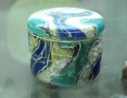 PYX-4018 - Pyxide en verre mosaïquéverreTPQ : -30 - TAQ : 50Pyxide cylindrique moulée à paroi rectiligne, ressaut sommital pour un couvercle débordant, également cylindrique, à sommet plat et lisse ; verre coloré, marbré, parfois avec inclusions de feuilles d'or; décor de cercles effectués au tour. 