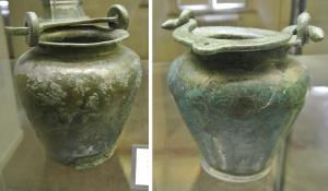 SIT-3019 - Situle stamnoïdebronzeSitule stamnoïde, à col étranglé et lèvre déversée; les attaches d'anses consistent en deux gros anneaux coulés sur le bord du vase en même temps que lui; anse plate et coulée, épaisse, avec un anneau de suspension centré.