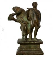 ACH-4035 - Applique de charbronzeFigurine plastique sur socle quadrangulaire, ouvert à l'arrière et par-dessous : deux personnages (Mois ?) debout, l'un présentant un panier ou une coupe de fruits, l'autre avec un outil sur l'épaule. Barre de renfort derrière les figurines.