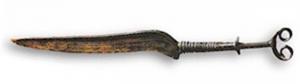 CTO-1054 - Couteau à manche massifbronzeCouteau à manche massif mais rapporté sur la soie de la lame, généralement en deux parties séparées par une moulure, et terminé par une paire de volutes; lame à dos sinusoïdal, orné d'incisions, et à pointe effilée; les plats peuvent être ornés d'incisions géométriques.