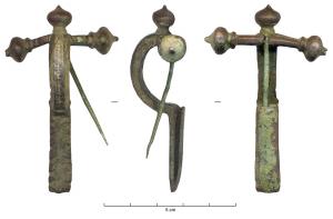 FIB-4261 - Fibule cruciformebronzeFibule cruciforme ; le bras transversal est épaulé, les bulbes sont en forme d'oignons et le pied décoré de plans inclinés vers l'extérieur ; l'arc comporte un sillon médian longitudinal.