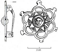 FIB-4864 - Fibule géométrique platebronzeFibule à charnière composée de deux plaquettes reliées par un axe en fer; la plaque circulaire, est ornée d'un bouton riveté, figurant un visage de face, au centre d'un décor en étoile et ponctué sur l'extérieur des branches; sur le pourtour, on trouve six 