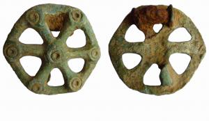 FIB-5143 - Fibule discoïdalebronzeFibule en forme de rouelle à 6 rayons, le centre du moyeu et les intersections avec la jante sont marqués de cercles oculés. Au revers, ressort en fer monté sur axe entre deux plaquettes.
