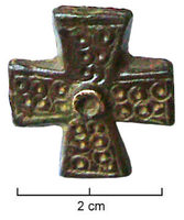 FIB-6010 - Fibule cruciformebronzeFibule en forme de croix latine, aux branches plates légèrement évasées vers leurs extrémités; surface couverte d'ocelles, autour d'un cabochon central.