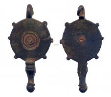 PDH-4118 - Pendant de harnaisbronzePendant à charnière, constitué d'un disque plat, orné d'un motif central de cercles concentriques, avec un ornement riveté; petites protubérances sur le pourtour; en guise de lest, pied mouluré terminé par un bouton.