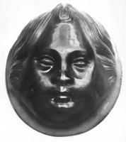PHA-4003 - Phalère : tête d'enfantpierre dureMédaillon en calcédoine, en fort relief, percé dans l'épaisseur de deux orifices se croisant à angle droit. Il figure  un visage enfantin, soit réaliste (corymbe), soit stylisé avec des traits épatés.