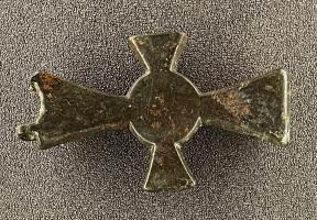 PLB-5688 - Plaque-boucle articulée à motif cruciformebronzePlaque-boucle articulée à motif cruciforme. Forme de croix latine. Boucle rectangulaire avec ardillon. Trois excroissances en arc de cercle par branche de la croix. Décor particulier composé de deux inscriptions, deux bustes et des formes géométriques. 