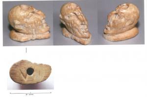 AML-4045 - Amulette/Pendeloque : tête grotesque en ososTête masculine en os reposant sur un socle plan. 
Visage dissymétrique, yeux enfoncés et fermés, nez busqué, bouche marquée par deux bourrelets, menton pointu, une oreille arrondie et une autre pointue, crâne chauve et arrondi ; 
Perforation traversant le crâne verticalement, et chiffre 